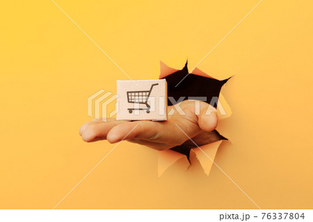 Hand with a delivery box through a yellow paper hole 76337804