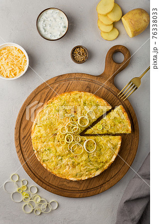 Quiche pie with leek, potatoes and cheese flat lay on gray concrete background and ingredients cheese, sour cream, onion rings on round wooden cutting board 76338033