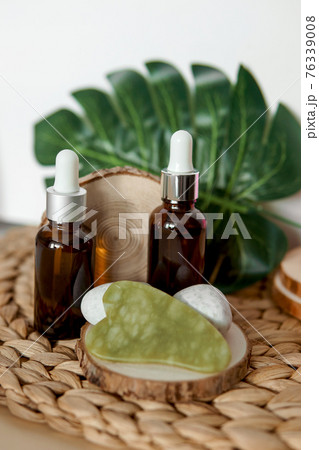 Jade Gua sha scraper and bottles of cosmetic serum for the face on wooden stands. Jade Gua sha scraper and bottles of cosmetic serum for the face on wooden stands. 76339008