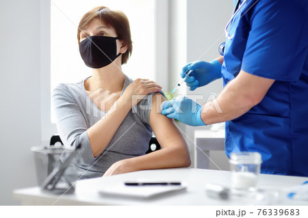 Doctor or nurse is preparing to give a injection vaccine against covid-19 to a woman. Mass vaccination. Herd immunity Doctor or nurse is preparing to give a injection vaccine against covid-19 to a woman. Mass vaccination. Herd immunity 76339683