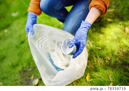 Volunteer picking up the plastic garbage and putting it in biodegradable trash-bag on outdoors. Ecology, recycling and protection of nature. Environmental protection. 76339719
