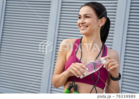 Smiling sporty brunette opening a water bottle Smiling sporty brunette opening a water bottle 76339989