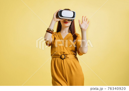 Excited young Caucasian woman in VR headset touching air exploring virtual reality at studio yellow background. Pretty lady enjoying artificial computer world or playing video game Excited young Caucasian woman in VR headset touching air exploring virtual reality at studio yellow background. Pretty lady enjoying artificial computer world or playing video game 76340920