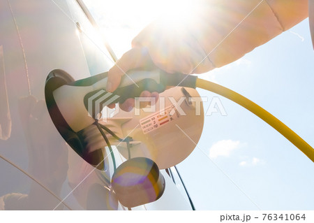 Close up woman hand inserts power cable supply to charge electric or EV car at sunlight Close up woman hand inserts power cable supply to charge electric or EV car at sunlight 76341064