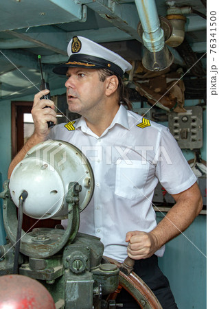 Captain standing in the wheelhouse is steering the ship with a rudder. 76341500
