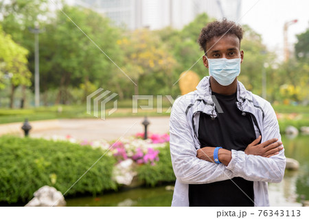 Portrait of handsome black African man wearing face mask with arms crossed 76343113