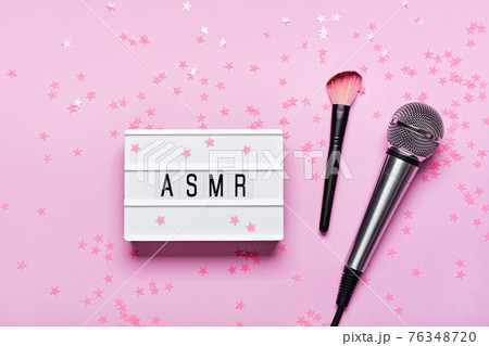 Microphone, brush and ASMR text lightbox on pink confetti background. ASMR recording stress relieving sounds concept, flat lay, trending shadows 76348720