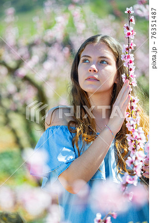 Portrait of young smiling woman in a garden with blooming peach trees Portrait of young smiling woman in a garden with blooming peach trees 76351487