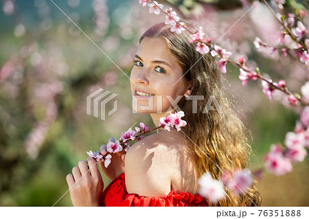 Cheerful girl posing in a red dress in spring blooming garde Cheerful girl posing in a red dress in spring blooming garde 76351888