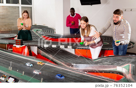 Cheerful men and women play together with slot car racing track Cheerful men and women play together with slot car racing track 76352104
