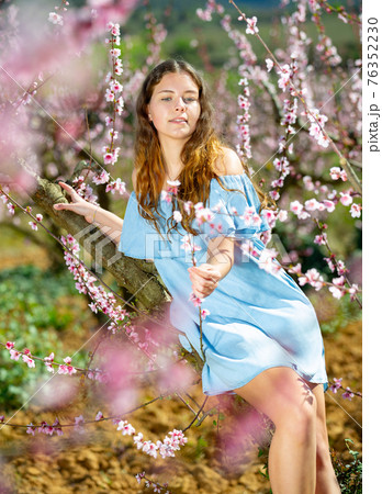 Portrait of young smiling woman in a garden with blooming peach trees Portrait of young smiling woman in a garden with blooming peach trees 76352230