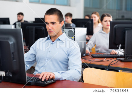 Group of people of different ages learning to use computers in classroom 76352343