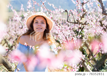 Portrait of young smiling woman in a garden with blooming peach 76352651