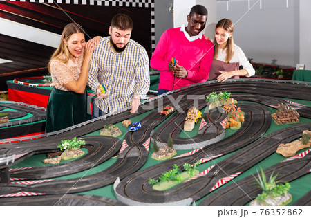 Happy friends enthusiastically remotely control car models on race track Happy friends enthusiastically remotely control car models on race track 76352862