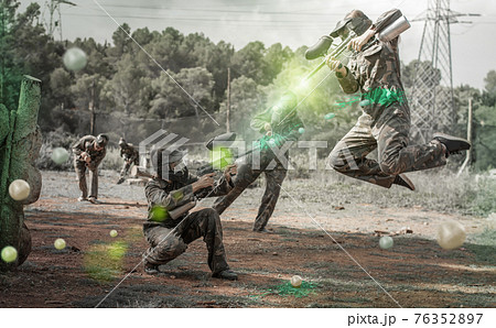 Dynamic paintball battle. Portrait woman player jumping and aimi Dynamic paintball battle. Portrait woman player jumping and aimi 76352897