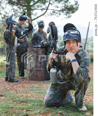Man wearing uniform and holding gun ready for playing with friends paintball outdoor Man wearing uniform and holding gun ready for playing with friends paintball outdoor 76352900