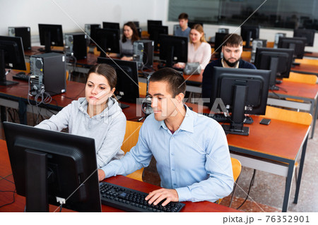 Computer science teacher supervises the execution of a programming task in a computer class 76352901