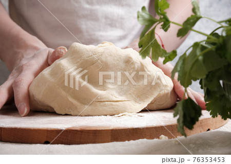 Women's hands knead the dough from wheat flour 76353453