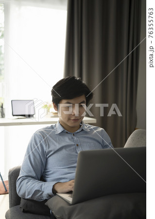 Portrait of happy casual man resting on comfortable sofa and using laptop computer. 76355763