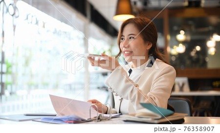 Confident businesswoman talking by speakerphone while sitting in modern office. Confident businesswoman talking by speakerphone while sitting in modern office. 76358907