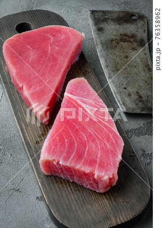Pieces of raw tuna fish, on wooden cutting board, and old butcher cleaver knife, on gray stone background Pieces of raw tuna fish, on wooden cutting board, and old butcher cleaver knife, on gray stone background 76358962