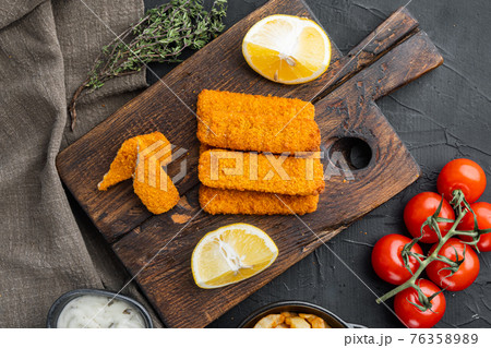 Fried fish finger stick or french fries fish with sauce, on wooden cutting board , on black background , on black wooden table background, top view flat lay Fried fish finger stick or french fries fish with sauce, on wooden cutting board , on black background , on black wooden table background, top view flat lay 76358989
