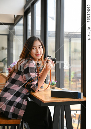 Portrait of cheerful young female photographer holding her digital camera and smiling to camera. 76359849
