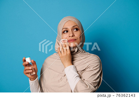Beautiful Muslim woman with covered head in hijab applying micellar lotion and removing make up from her lips 76362143
