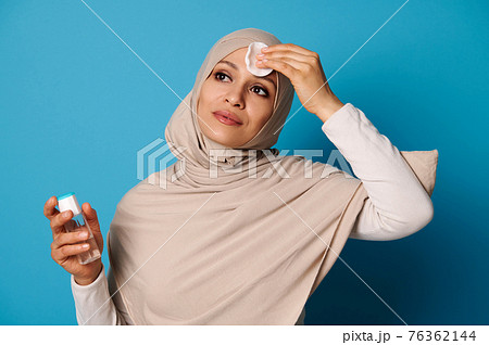 Attractive muslim woman removing makeup from her face using micellar water and cotton pad. Skin care concepts Attractive muslim woman removing makeup from her face using micellar water and cotton pad. Skin care concepts 76362144