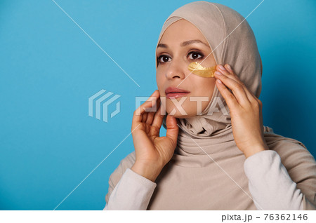 Closeup of Muslim woman in hijab using hydrogel eye patches. Beauty portrait on blue background with copy space 76362146