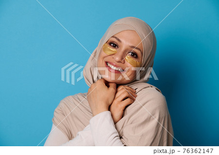 Beautiful woman with covered head in hijab, smiling at camera with hydrogel collagen patches under eyes 76362147
