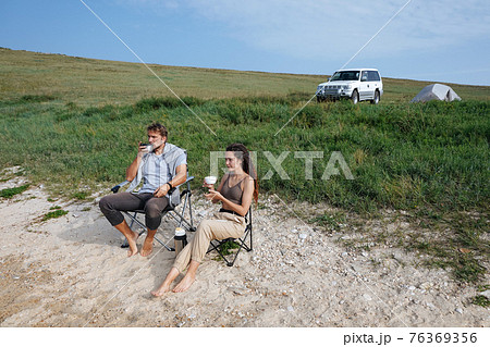 Couple sits on the shore and drinks from a thermos Couple sits on the shore and drinks from a thermos 76369356