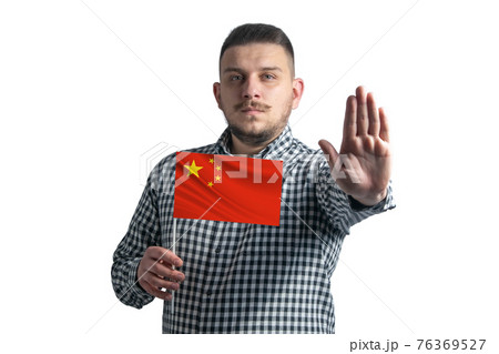 White guy holding a flag of People's Republic of China and with a serious face shows a hand stop sign isolated on a white background 76369527