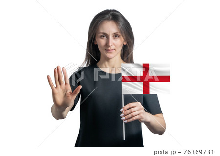 Happy young white woman holding flag of England and with a serious face shows a hand stop sign isolated on a white background Happy young white woman holding flag of England and with a serious face shows a hand stop sign isolated on a white background 76369731