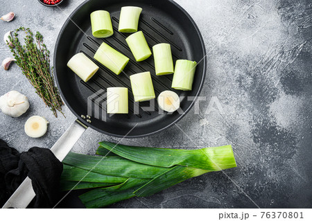 Raw braised Leeks on grill pan uncooked with herbs ingredients , on textured grey background top view with space for text. Raw braised Leeks on grill pan uncooked with herbs ingredients , on textured grey background top view with space for text. 76370801