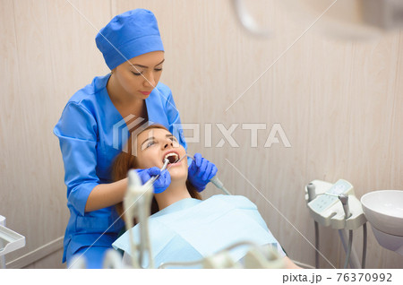 Dental inspection in clinic. Doctor in uniform checking up female patient's teeth in dental clinic. 76370992