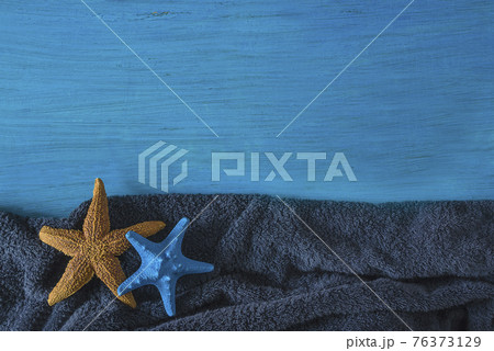 Summer beach holidays concept. Frame of two starfishess on dark blue beach towel and blue paint wooden background. Space for text 76373129