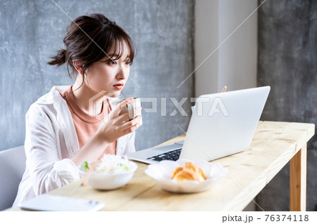 朝食でノートパソコンを使う若い女性 朝食でノートパソコンを使う若い女性 76374118