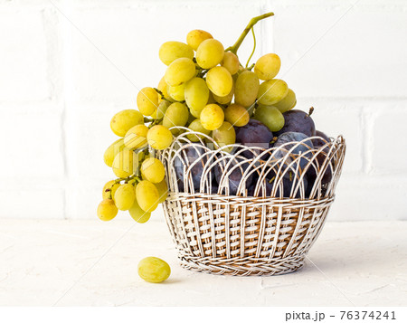 Just picked plums and grapes in wicker basket on white backdrop. 76374241