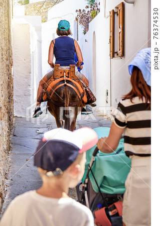 Tourists riding donkeys with leather saddles on paved road 76374530