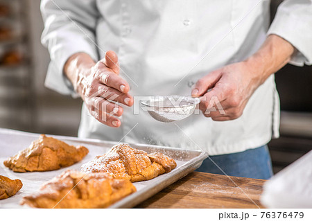 Male hands sprinkling confectionery with powdered sugar Male hands sprinkling confectionery with powdered sugar 76376479