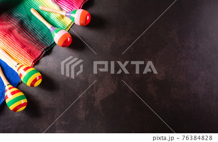 Cinco de Mayo holiday background made from maracas, mexican blanket stripes or poncho serape on dark stone background. 76384828