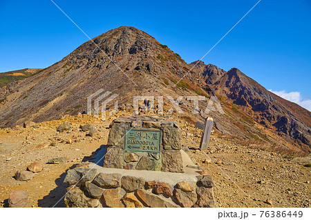 秋の栃木県那須岳の峰の茶屋避難小屋前の道標越しに剣が峰、朝日岳方面を見る 76386449