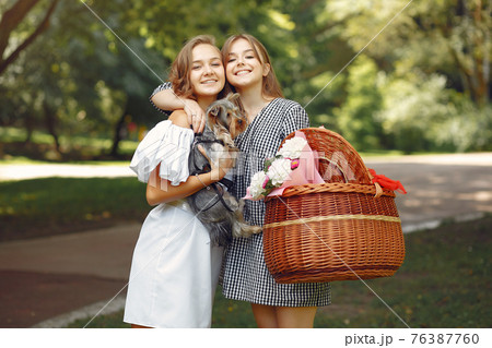 Two cute girls in a park playing with little dog Two cute girls in a park playing with little dog 76387760