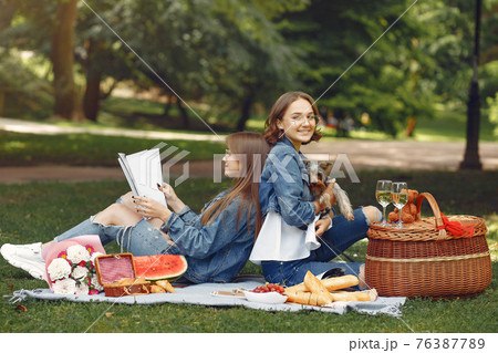 Two cute girls in a park playing with little dog 76387789