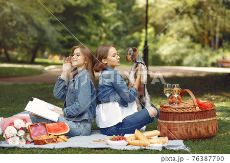 Two cute girls in a park playing with little dog Two cute girls in a park playing with little dog 76387790