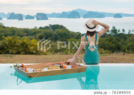 Happy young woman in green swimsuit having Floating Breakfast tray in luxury pool hotel, girl with hat enjoy in tropical resort. Relaxing, Exotic summer travel, holiday, vacation and tropical 76389950