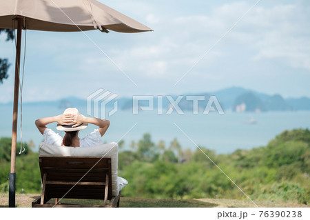 Happy traveler in white dress and hat enjoy beautiful sea view, young woman sitting on chair and looking ocean at tropical beach. Freedom, relaxing, vacation holiday and summer travel concept Happy traveler in white dress and hat enjoy beautiful sea view, young woman sitting on chair and looking ocean at tropical beach. Freedom, relaxing, vacation holiday and summer travel concept 76390238