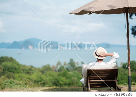 Happy traveler in white shirt and hat enjoy beautiful sea view, young man sitting on chair and looking ocean at tropical beach. Freedom, relaxing, vacation holiday and summer travel concept Happy traveler in white shirt and hat enjoy beautiful sea view, young man sitting on chair and looking ocean at tropical beach. Freedom, relaxing, vacation holiday and summer travel concept 76390239