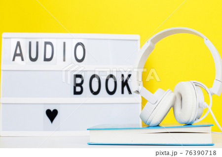 Audio book concept with modern white headphones and hardcover book on a yellow background. inscription on a lightbox Audio book concept with modern white headphones and hardcover book on a yellow background. inscription on a lightbox 76390718